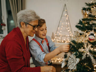 An older woman helps a young boy hang an ornament on a Christmas tree.